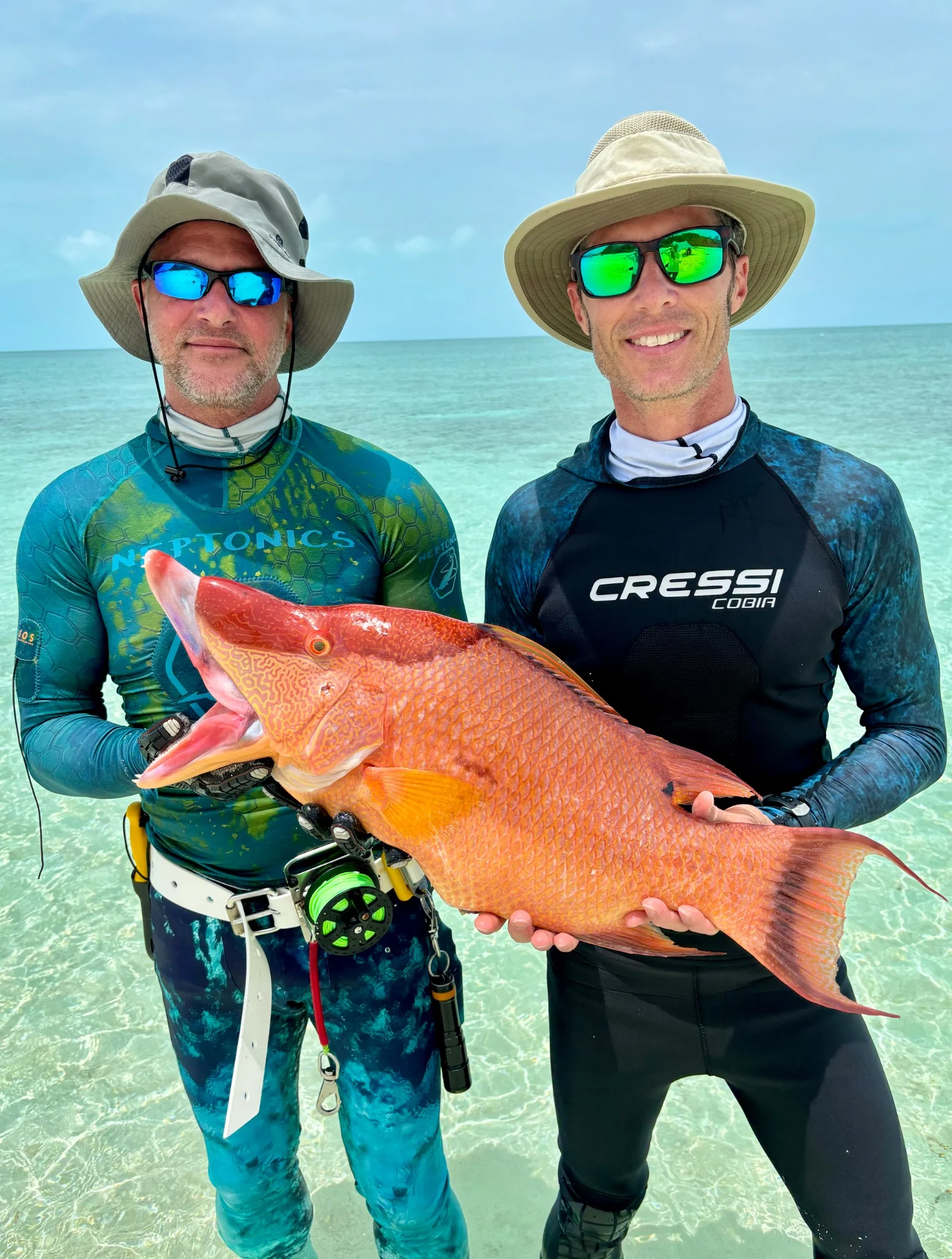 A diver standing by the water with a large hogfish catch